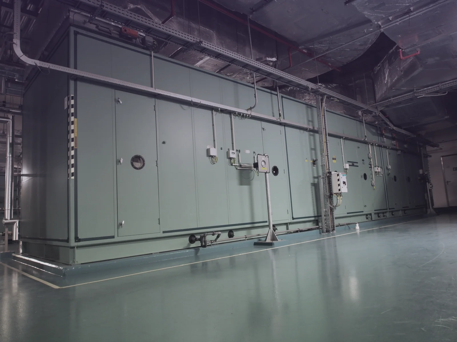 A long green air handling unit in a commercial mechanical room.
